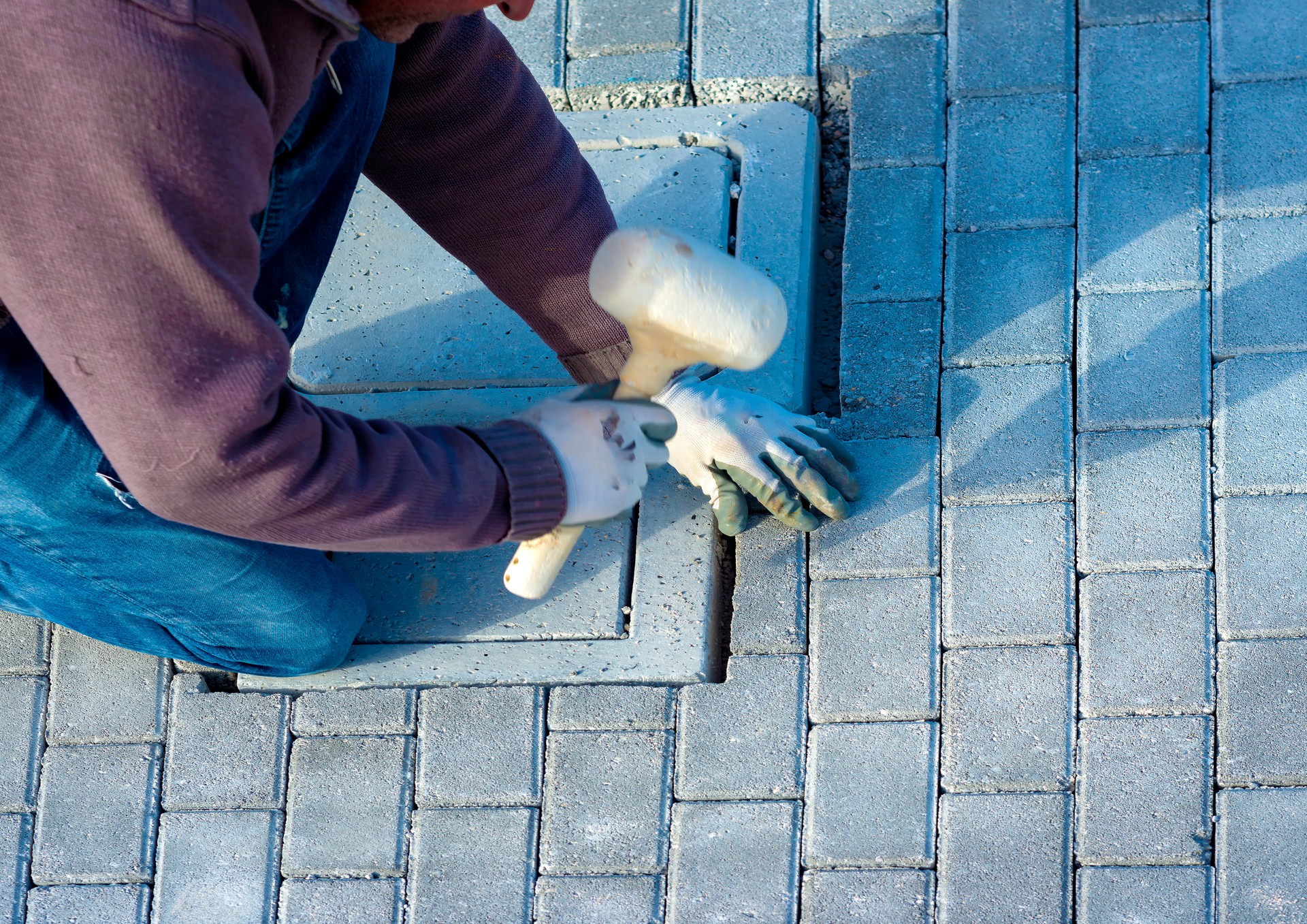 Construction worker laying interlocking paving concrete onto sheet nonwoven bedding sand and fitting them into place.